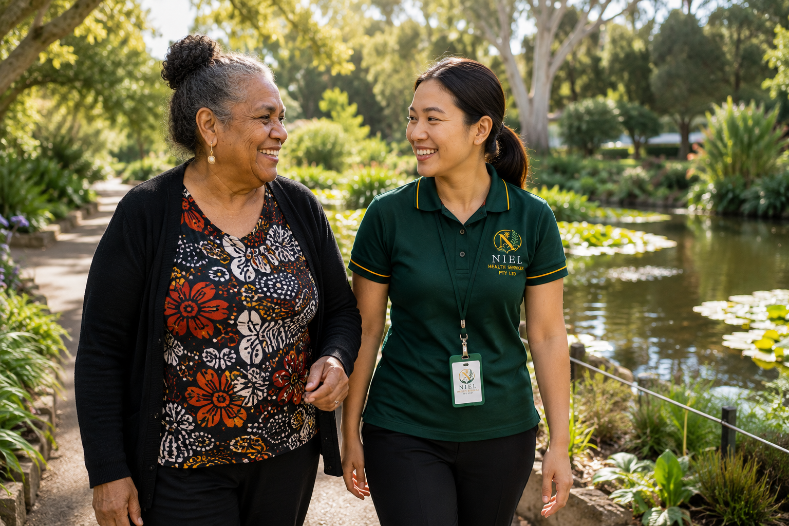 A Niel Health Services support worker in an emerald green polo walks alongside an older participant in a beautiful botanical garden, sharing conversation and companionship